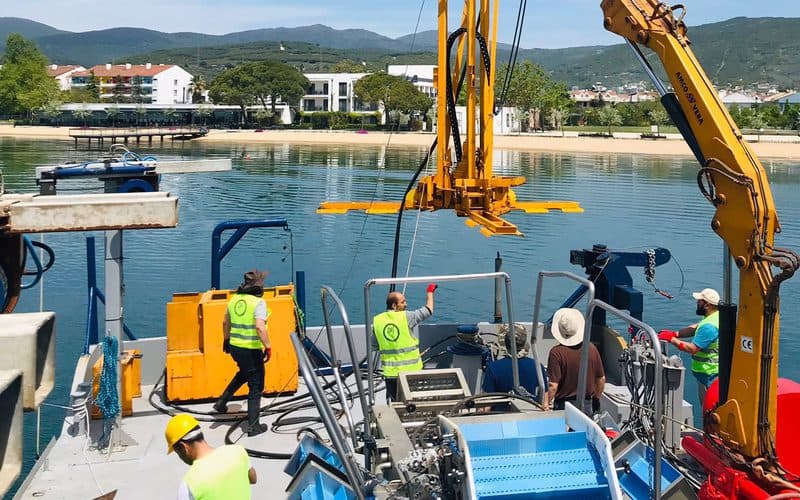 Deck-mounted drive rig being lowered from a work vessel to install screw anchors in shallow water